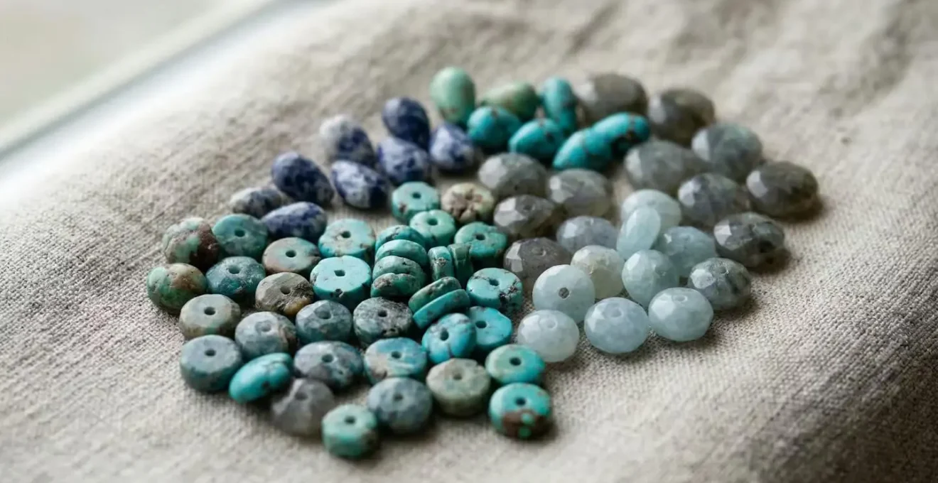 Différentes formes de perles en pierre naturelle : heishis, rondelles facettées et gouttes sur tissu lin